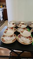 Six Royal Albert Old Country Roses teacups and matching saucers arranged on a black table.