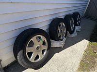 Four tires mounted on silver Volvo rims, placed upright against white siding in outdoor area.