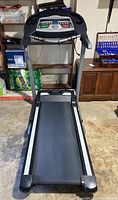 Full treadmill from front showing belt and control panel with buttons and handles, stored in garage area.