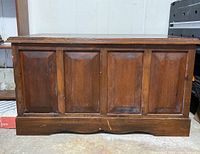 Front view of wooden storage chest showing four recessed panels and a molded base with scratches.
