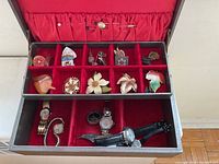 Top view of red velvet-lined jewelry box showing assorted pins, brooches, rings, and four wristwatches in two section trays.