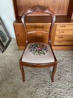 Front view of the wooden Queen Anne style chair showing carved backrest and floral needlepoint seat upholstery.