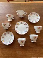 Full view of all tea set items arranged on wood table, includes 6 cups, 6 saucers, 6 plates, and 1 creamer.