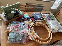 Top view of vintage Singer sewing machine and various sewing supplies including embroidery hoops, yarn, fabric, and patterns laid out on a wooden table.