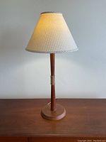 Full view of the wooden table lamp on a wooden surface, showing the lamp turned on with the cream-colored, textured fabric lampshade and round wooden base.