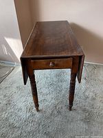 Front view of wood drop leaf table showing drawer and turned legs