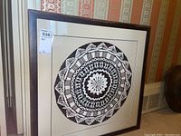 Full view of framed Tapa cloth artwork showing circular geometric and figure patterns in black and white within a dark wood frame and white matte.