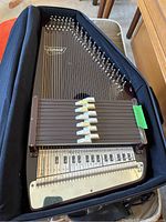 Oscar Schmidt autoharp in its open black carrying case with visible strings and chord bars.