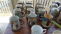12 Beswick ceramic beer mugs with colorful relief scenes from A Christmas Carol arranged in rows on table.