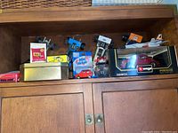 Model cars and toy cars of various sizes on wooden shelf, including blue race cars, boxed red Porsche 356B, and small boxed and loose toys.