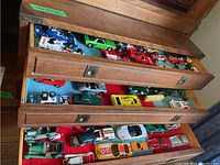 Three wooden drawers pulled out showing assorted diecast cars on felt