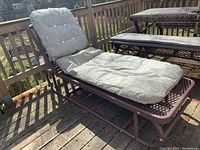 Metal chaise lounge showing the full lounge with cushion in an outdoor setting on a wood deck.
