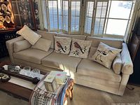 Full view of beige three-seat sofa with four accent pillows in front of shuttered windows