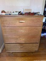 Front view of wood dresser with four drawers showing wood grain, finish damage around handles, and rounded feet.