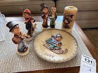 Full view of all items: three Hummel figurines, 1975 plate, and candle.