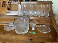 Five tumblers lined up behind ice bucket, vase, bowl, and trinket dish on wooden surface