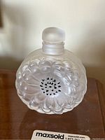 Front view of frosted glass bottle showing floral relief pattern and rounded stopper.