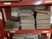 Photo of large stacks of magazines on red metal shelving, showing many issues in thick piles.