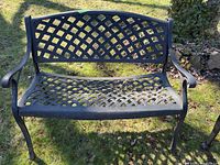 Front view of black metal patio bench with lattice pattern on seat and backrest, showing outdoor setting on grass.