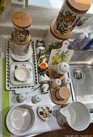 Top-down view of entire ceramic kitchenware set on countertop showing canisters, trays, salt and pepper shakers, rolling pin, and bowl with fruit patterns.