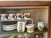 Full shelf showing mugs, plates, bowls, and creamers with fruit designs