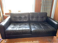 Full view of the black leather sofa with tufted cushions and metal legs.