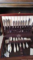 Fitted wood case open showing rows of dinner knives in upper rack and assorted forks and spoons in lower compartment
