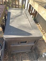 Suncast DBW7500 brown plastic deck storage box placed outdoors on wooden deck near railing.