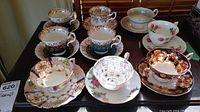 Seven assorted vintage porcelain teacups and saucers on a table, various floral and patterned designs.