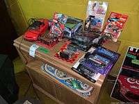Overview of table with various packaged toy cars including Muscle Machines and James Bond 007 models and the NASCAR poster leaning against the wall