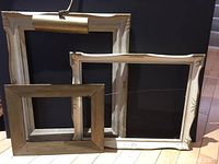 Three antique picture frames including one large frame with attached brass light fixture, all set against a black backdrop on wood floor.