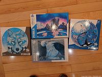 Four unopened Indigenous art puzzles displayed on a wooden floor showing wolf, orca, eagle, and buffalo themes.