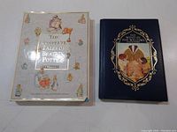 Two hardcover children's books: The Complete Tales of Beatrix Potter with a white illustrated cover and The Wind in the Willows with a navy blue cover and framed illustration