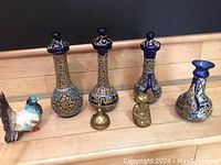 Five ceramic vases/decanters with blue and gold patterns, two small brass figurines, and a decorative bird figurine displayed on wooden surface