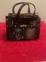 Front view of David Jones purse showing flap with leopard print suede and reptile embossed leather, gold-tone turn-lock closure, and two carrying handles.