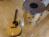 Marlin acoustic guitar and two Pearl drums on hardwood floor from an angled top-down view.
