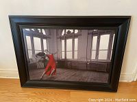 Framed large artwork of dancer in red dress, standing in a vintage room with large windows and wooden floors.