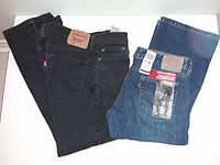 Two pairs of Levi's jeans laid side by side on a white surface, one black and one blue pair with tags visible on the blue jeans.