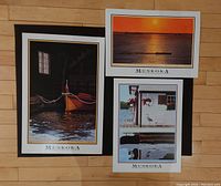 Photo of three framed Muskoka art prints by D.A. Dunford showing various Muskoka scenes: a boat in a boathouse, a boat on the water at sunset, and a heron by a cottage.