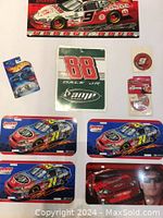 Overall view of assorted NASCAR memorabilia items including metal and laminated plates and a Hot Wheels car pack, arranged on white background.