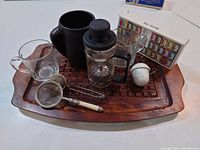 Wooden tray holding tea set including teapot, glass cup, French press, two strainers, tea infuser, and tea bag box