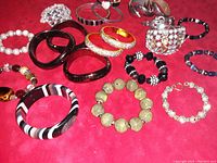 Multiple vintage costume bracelets of various designs and sizes laid on red fabric showing different materials like resin, beads, enamel, and rhinestones.