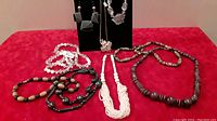 Wooden and beaded necklaces arranged on a red surface with some necklaces lying down and others hanging on a black velvet display stand.