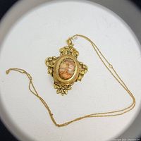 Close-up photo of gold-filled chain with antique Art Nouveau style locket pendant showing intricate floral and scroll design and marbled oval stone.