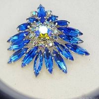 Close-up photo of a 1950s Austrian crystal brooch with blue marquise crystals and a cluster of smaller clear crystals in the center, set in silver-tone metal on a white background.
