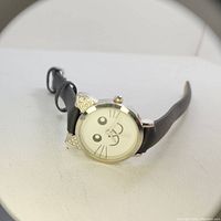 A girls cat face watch with black strap shown frontally under a ring light view, highlighting the round gold-tone case accented with cat ears and the cute cat face dial.