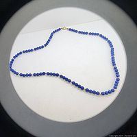 Photo of full length of lapis lazuli bead necklace laid out flat on white surface.