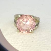 Close-up photo of large pink faceted round stone ring with visible prongs and silver-tone band.