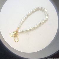 Pearl beaded keychain with white round faux pearls and gold-tone metal hardware. Photo shows curved loop formation.