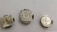 Three Swiss watch movements shown side by side, including two square Nivrel branded pieces and one round Simon branded piece.
